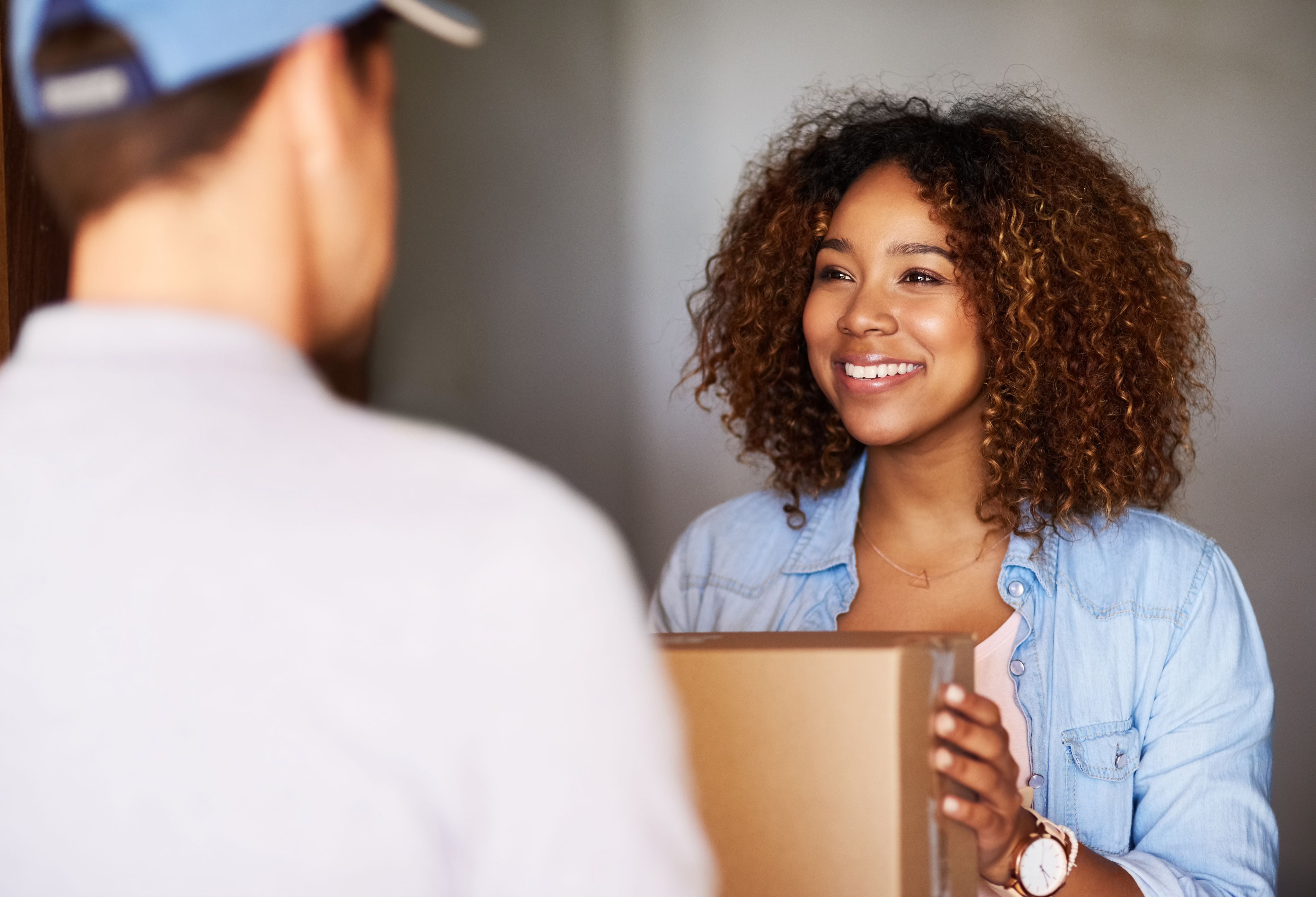 Smiling woman receiving package at door — shipment delivery imagery.
