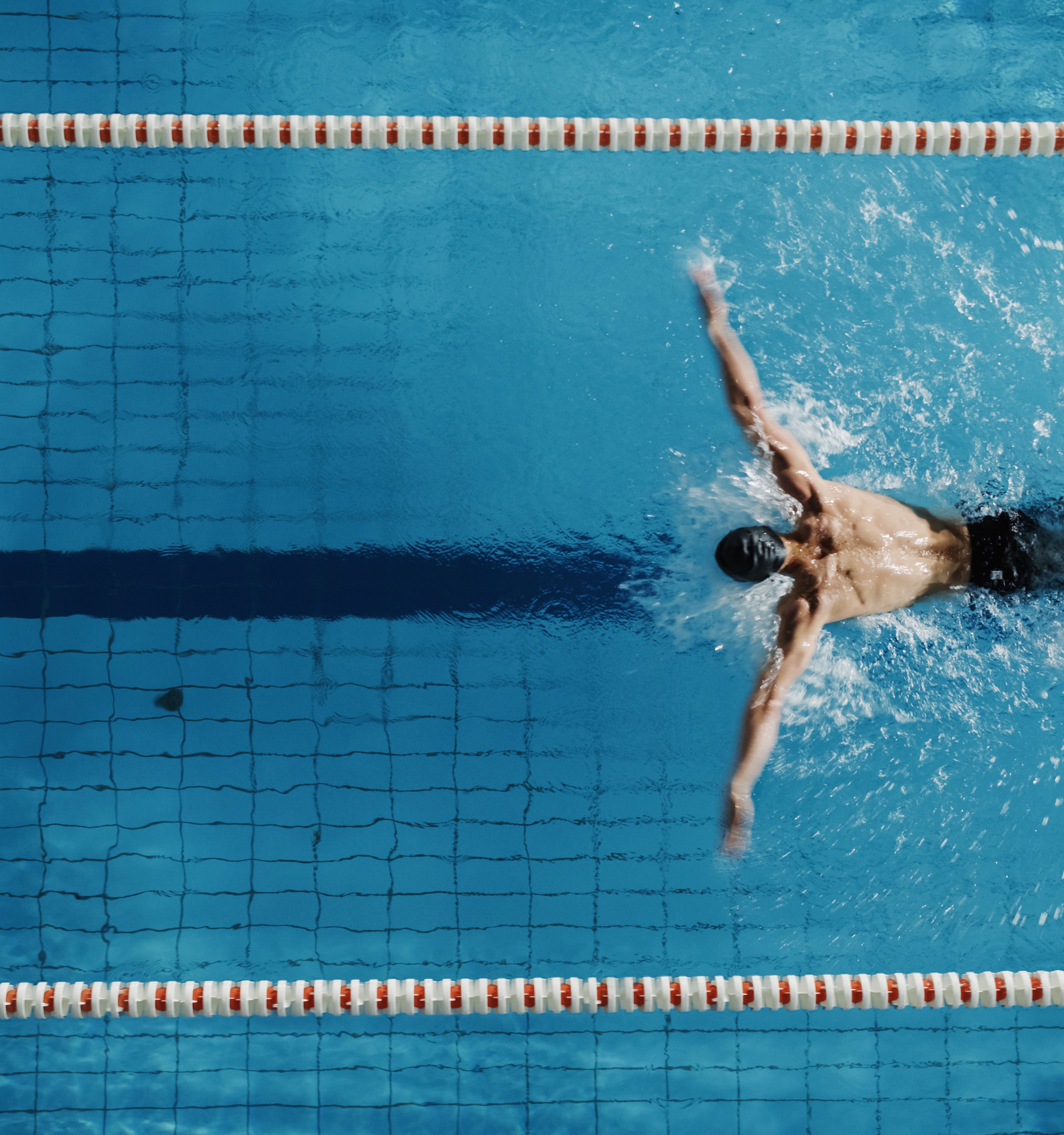 Swimmer mid-stroke in a lap pool — testimonial portrait for Jon, peptide patient.